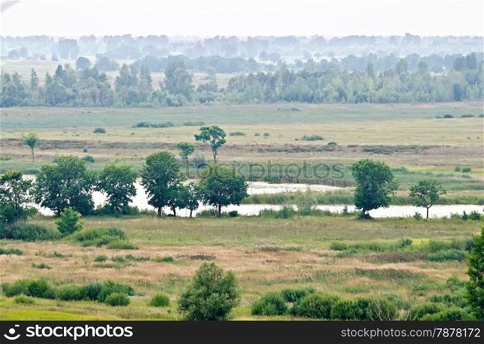 Landscape with small river, trees, field, forest and sky in the background