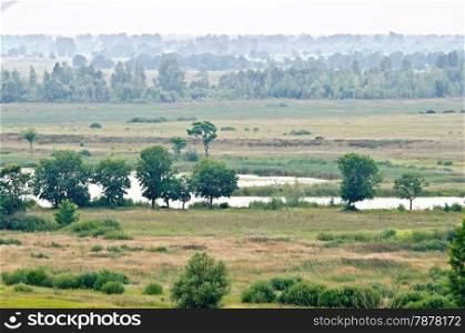 Landscape with small river, trees, field, forest and sky in the background