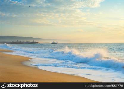 Landscape with the ocean beach, fishing ship at beautiful sunset. Nazare, Portugal