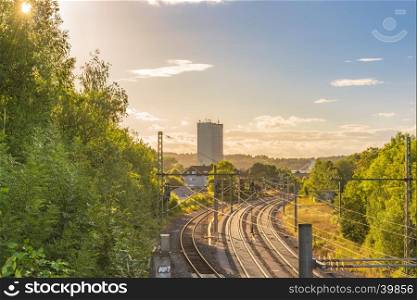 Landscape with the sun rays passing through the green trees and enlightening the railways and the industrial buildings that lies on the horizon.