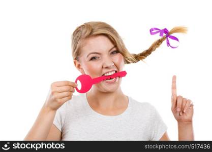 Language barrier concept. Teenage blonde girl with braid hair biting big pink key pointing at something. Teenage girl with braid biting key
