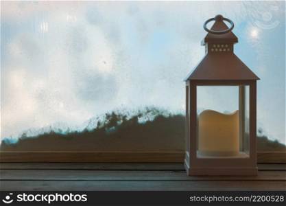 lantern with candle wood board near bank snow through window