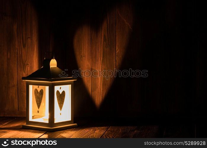 Lantern with heart shaped glass. Lantern with heart shaped glass and burning candle inside on wooden background with copyspace for Valentines or Christmas