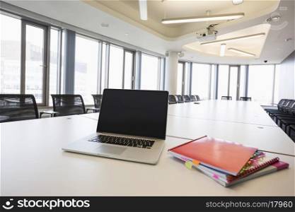 Laptop and files on empty conference table in creative office