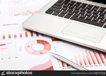laptop and pen with red business charts, graphs, information and reports background for financial and business concepts