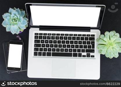Laptop and phone on black table mock up flat lay scene, copy space on blank screens. Offise desktop scene
