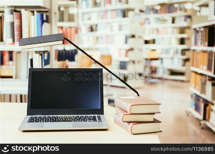 Laptop and pile of books on a wooden table. University library.