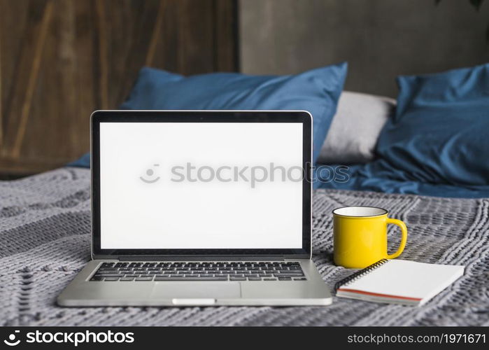 laptop blank white screen near cup spiral notepad bed. High resolution photo. laptop blank white screen near cup spiral notepad bed. High quality photo