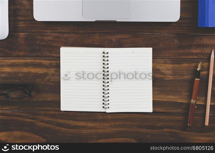 laptop computer and notepad on wooden office desk - top view