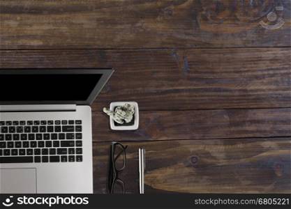 laptop computer, black eyeglasses, cactus pot and pen on wood office desk - top view