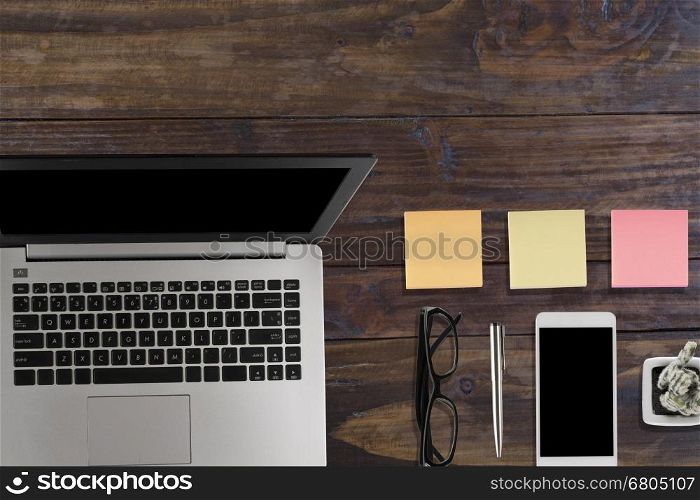 laptop computer, black eyeglasses, notepad, smartphone and pen on wood office desk - top view