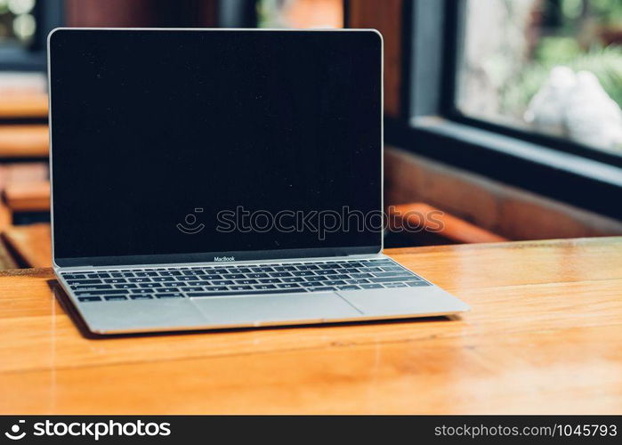 Laptop computer mockup with blank screen on desk in coffee shop.