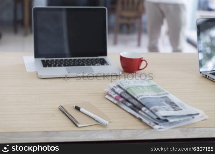 laptop computer, newspaper, notebook, pen and red coffee cup on wooden table for working concept