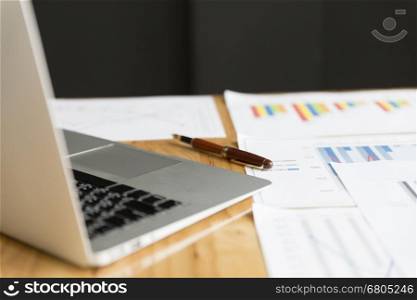 laptop computer, pen and market analysis business chart document on office desk