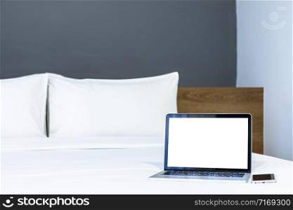 Laptop computer with blank screen with smart phone on white bed decoration in hotel bedroom interior background,Work and business in leisure with travel in the holiday concept.