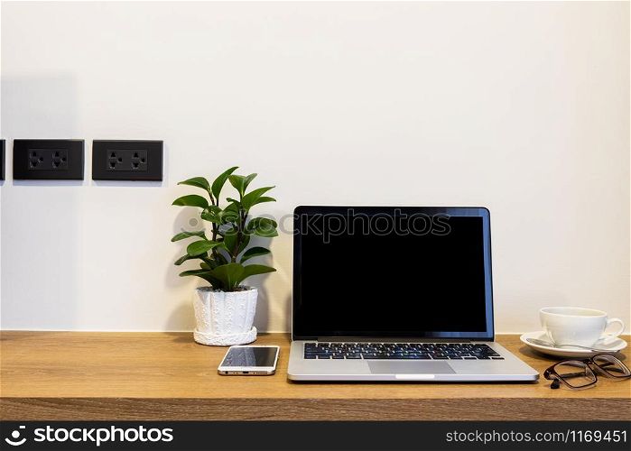 Laptop computer with blank screen with smart phone, spectacles and a coffee cup on brick wall on wooden table interior of room room hotel background,Work business in leisure with travel holiday