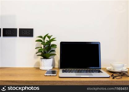 Laptop computer with blank screen with smart phone, spectacles and a coffee cup on brick wall on wooden table interior of room room hotel background,Work business in leisure with travel holiday