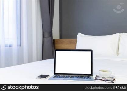 Laptop computer with blank white screen with smartphone,coffee cup and spectacles on white bed decoration in hotel bedroom interior background,Work and business in leisure with travel in the holiday.