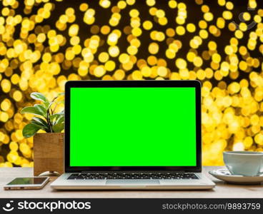 laptop computer with empty green screen with smartphone and coffee cup  on table Yellow Colorful light Abstract circular bokeh of Christmas tree background Decoration During Christmas and New Year