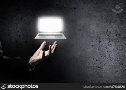 Laptop in male hand. Hand of businessman holding glowing laptop in palm