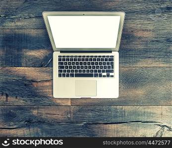 Laptop notebook with black screen on wooden desk. Office workspace background. Vintage style toned picture