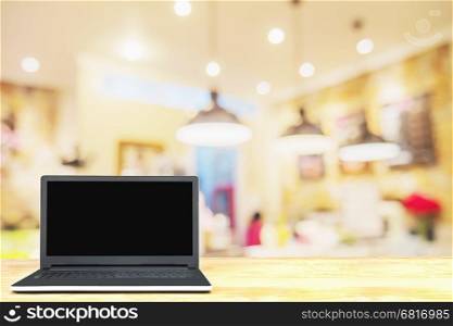Laptop on wooden table over blurred photo of beautiful coffee shop for background use