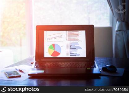 Laptop on wooden table showing charts and graph against office background ,Analysis Business Accounting, Statistic Concept. Vintage color filtered.
