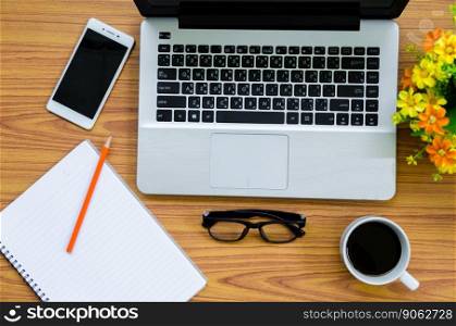 laptop on wooden table with coffee cup, phone, book and flower on top view