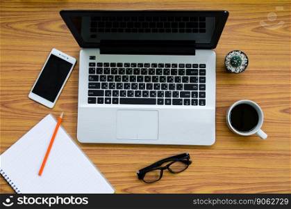 laptop on wooden table with coffee cup, phone, book, glasses and cactus on top view