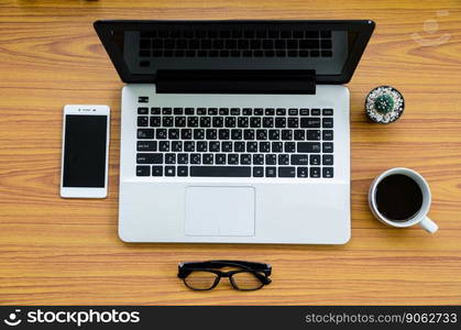 laptop on wooden table with coffee cup, phone, glasses and cactus on top view