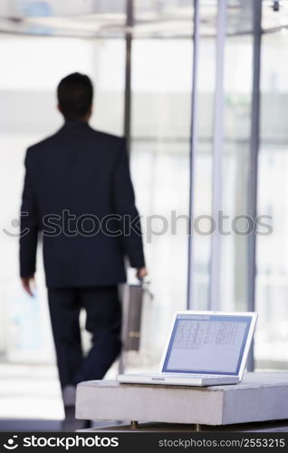 Laptop sitting on stone bench outdoors with businessman walking away in background (high key/selective focus)