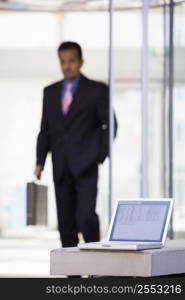 Laptop sitting on stone bench outdoors with businessman walking in background (high key/selective focus)