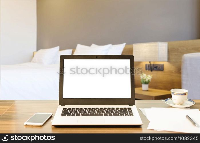 Laptop,smart phone and document on wooden table of defocused white pillow on bed decoration with light lamp in hotel bedroom interior background,Leisure and travel in the holiday concept.