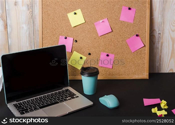 laptop takeaway coffee cup mouse corkboard with adhesive notes black desk