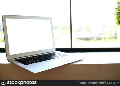 Laptop with blank screen on wooden table in front of window