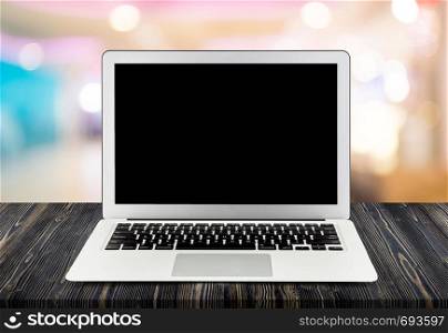Laptop with blank screen on wooden table on blur supermarket or department bokeh background, notebook computer display on wood desk, business concept.