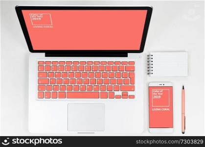 Laptop with living coral colored keyboard with smartphone and notebook, view from above. Laptop with smartphone