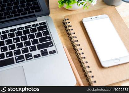 laptop with smartphone on notebook,a pencil and flower pot tree on wooden background,Top view office table.