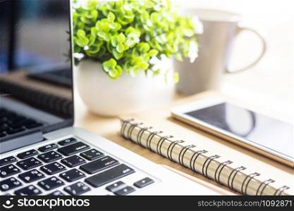 laptop with smartphone on notebook,a pencil and flower pot tree on wooden background,Top view office table.