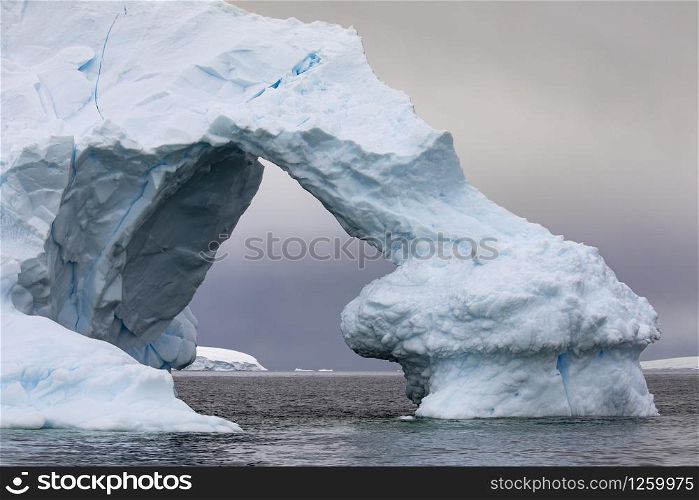 Large arch of ice as a gate through iceberg shimmers bluish close up