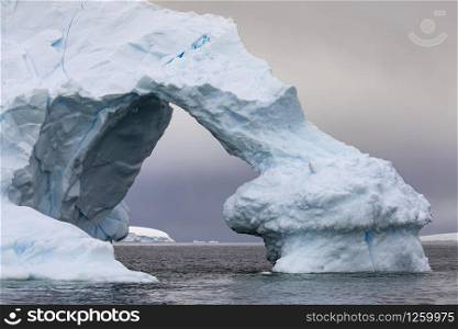 Large arch of ice as a gate through iceberg shimmers bluish close up