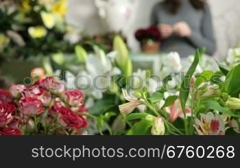 Large array of flowers in florist shop, in the background woman arranging Valentines Day rose heart bouquet. Dolly shot