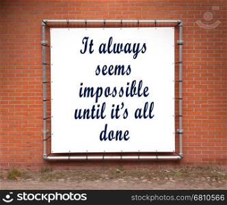 Large banner with inspirational quote on a brick wall - It always seems impossible until it's all done