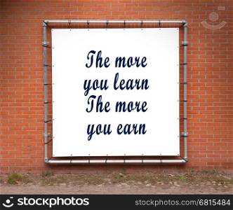 Large banner with inspirational quote on a brick wall - The more you learn the more you earn