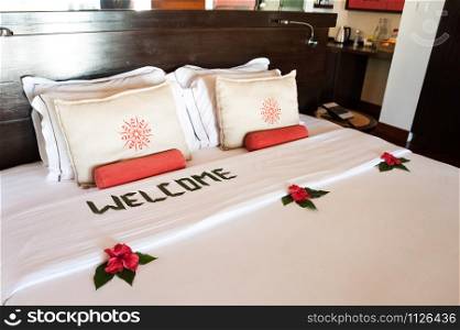 large bed with white pillows and a coverlet, decorated with tropical flowers and an inscription - welcome. Theme of hotel service, hotel, beach, rest