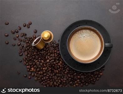 Large black coffee in porcelain cup with raw beans and capsules on brown.Top view.
