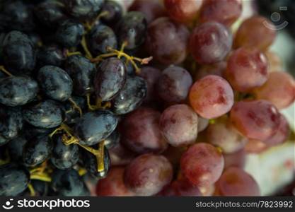 Large bunch of black and red grapes is placed in a dish. Sweet taste.