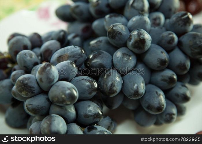 Large bunch of black grapes is placed in a dish. Sweet taste.