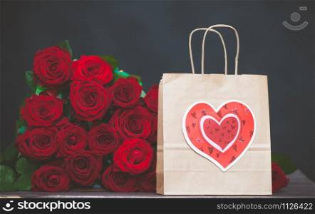 large bunch of red roses and a gift bag with a heart. The concept of a gift for Valentine&rsquo;s Day, love, wedding, date