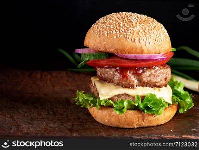 large burger with two fried cutlets, cheese and vegetables in a round wheat flour bun, copy space